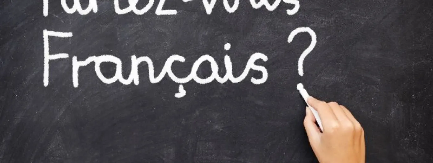 Foto de una mano que escribe con tiza en un tablero la frase "Parlez vous Français?"