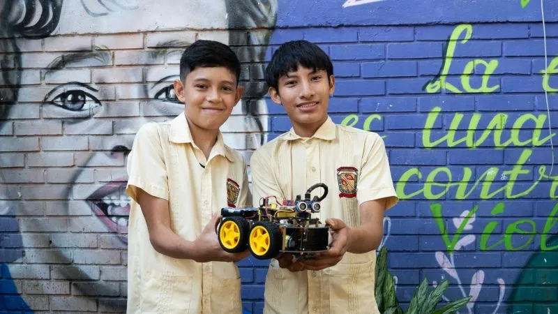 Los Centros de Interés avanzan en la formación del pensamiento crítico, creativo y computacional, en niños y jóvenes Foto de dos niños con uniforme amarillo sosteniendo un carro prototipo