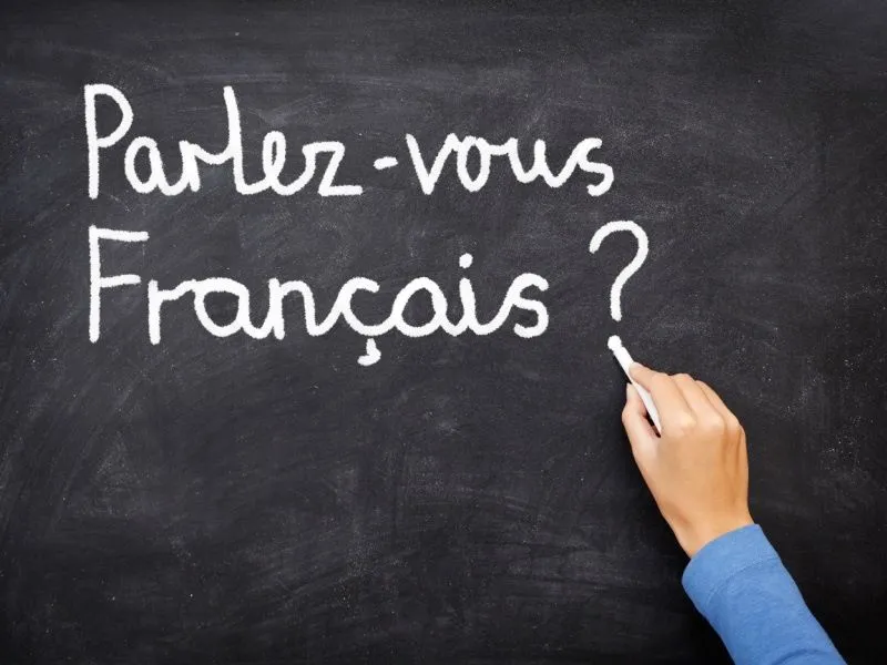 Foto de una mano que escribe con tiza en un tablero la frase "Parlez vous Français?"