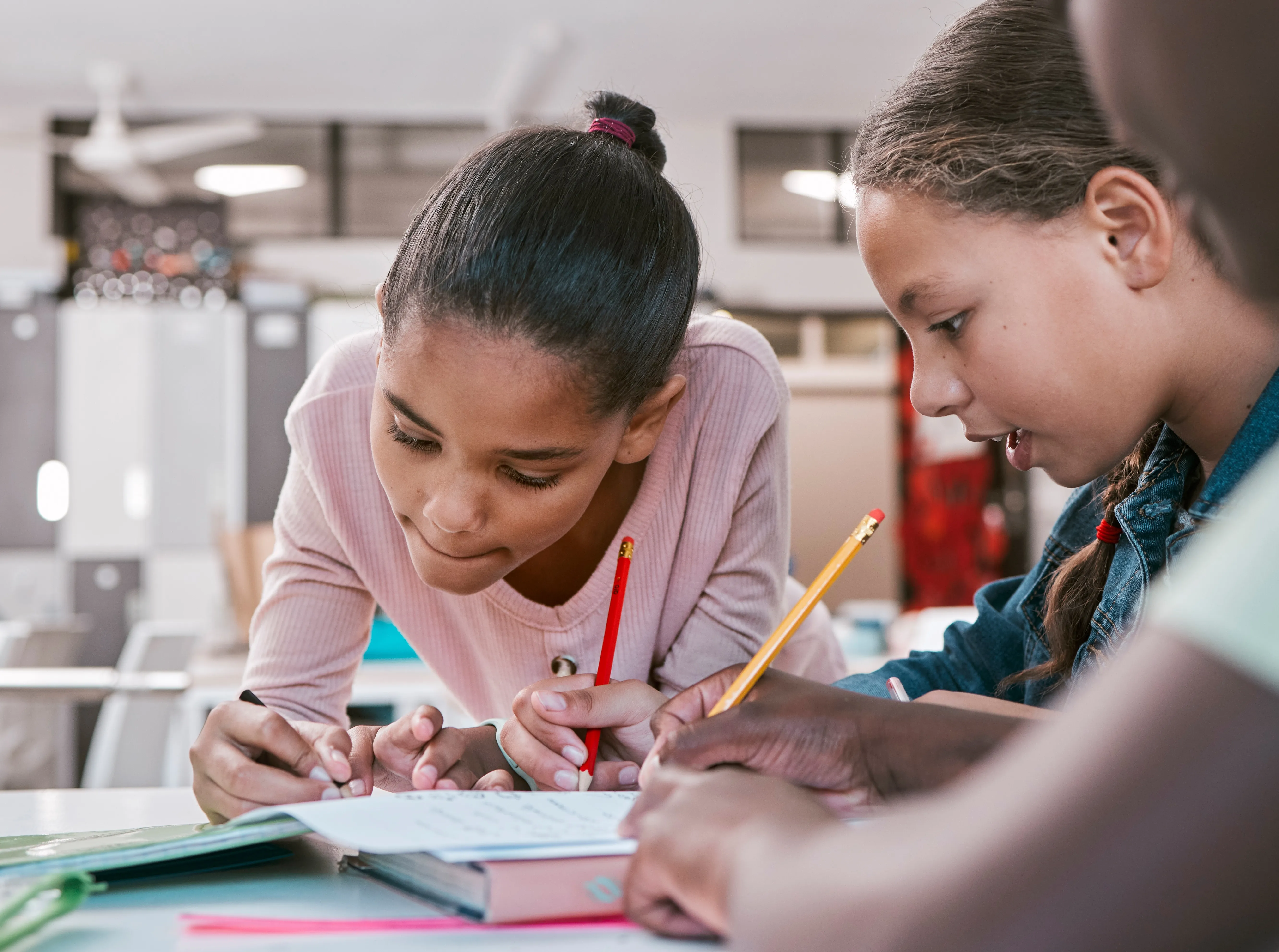 Fotografía principal del contenido 8 de septiembre Día Internacional de la Alfabetización. Tres niñas trabajan juntas en un salón de clases, escribiendo con lápiz en un cuaderno mientras comparten ideas y se concentran.