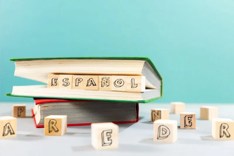 Fotos de dos libros y cubos con letras. El libro de encima tiene en la mitad cubos que forman la palabra "español"