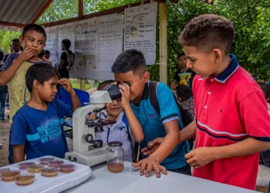 Grupo de cinco niños junto a un microscopio y uno de ellos mira a través del lente