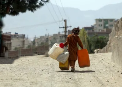 Foto de niña de espalda que camina en calle polvorienta con 4 recipientes grandes para recoger agua