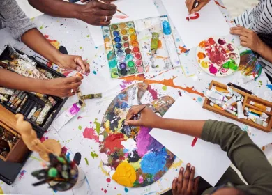 Manos de jóvenes en medio de acuarelas de colores creando arte